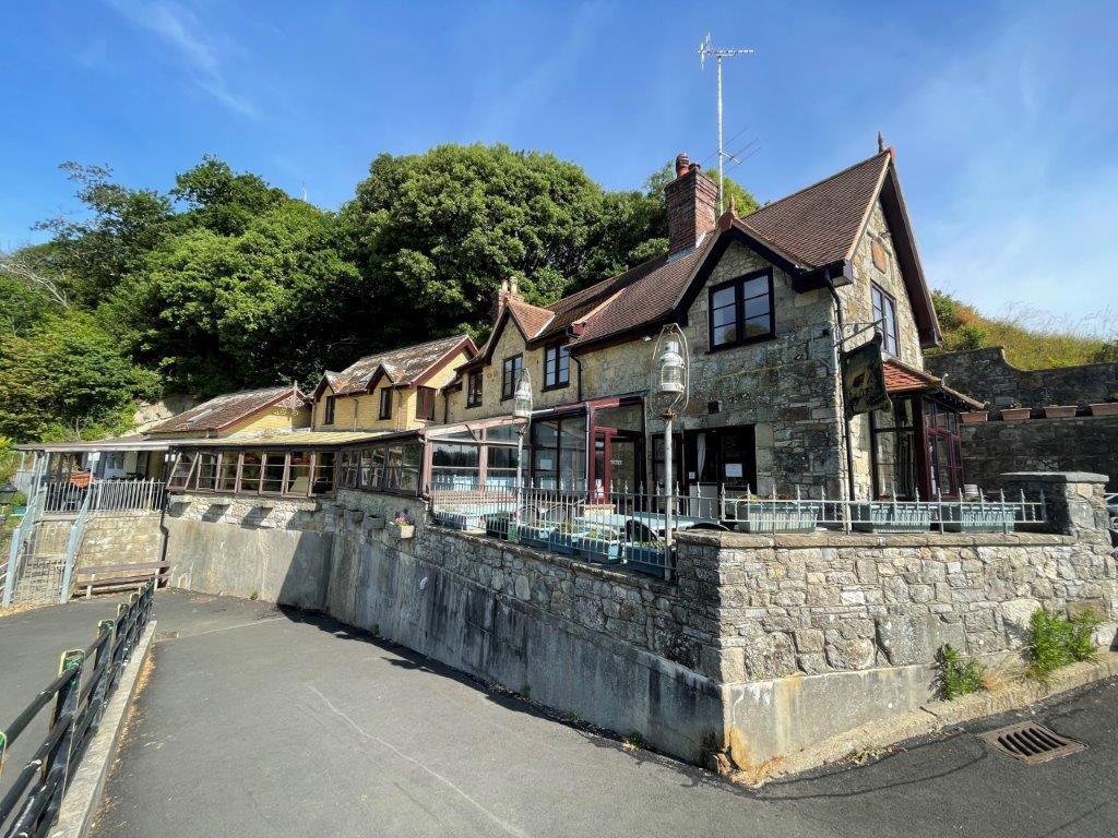 Lot: 98 - SEAFRONT PUBLIC HOUSE WITH STUNNING VIEWS AND OWNER/MANAGER LIVING ACCOMMODATION OVER - A View of the building from the coastal path